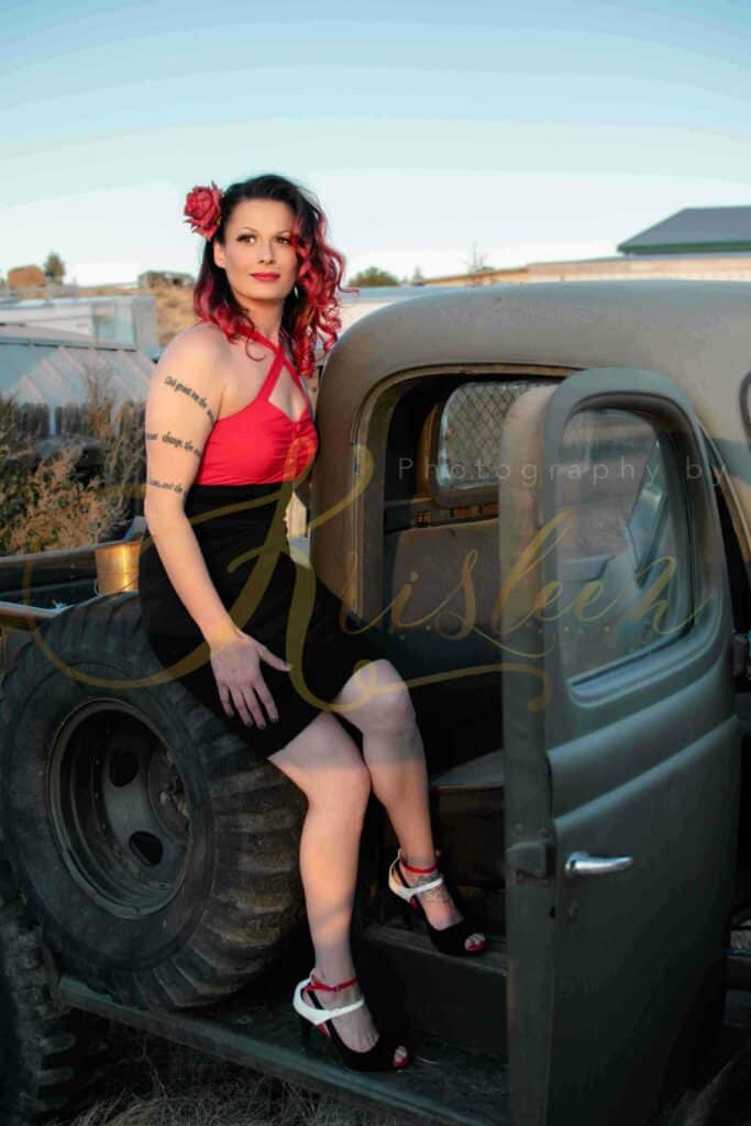 pin-up girl wearing a red rose in her hair and sitting on the bed of a classic pickup truck