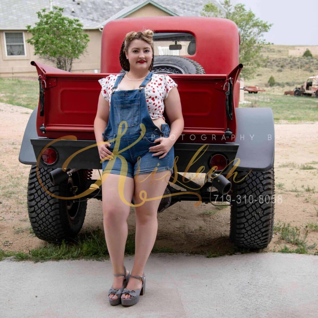 pin-up girl in denim overalls standing behind a classic pickup truck